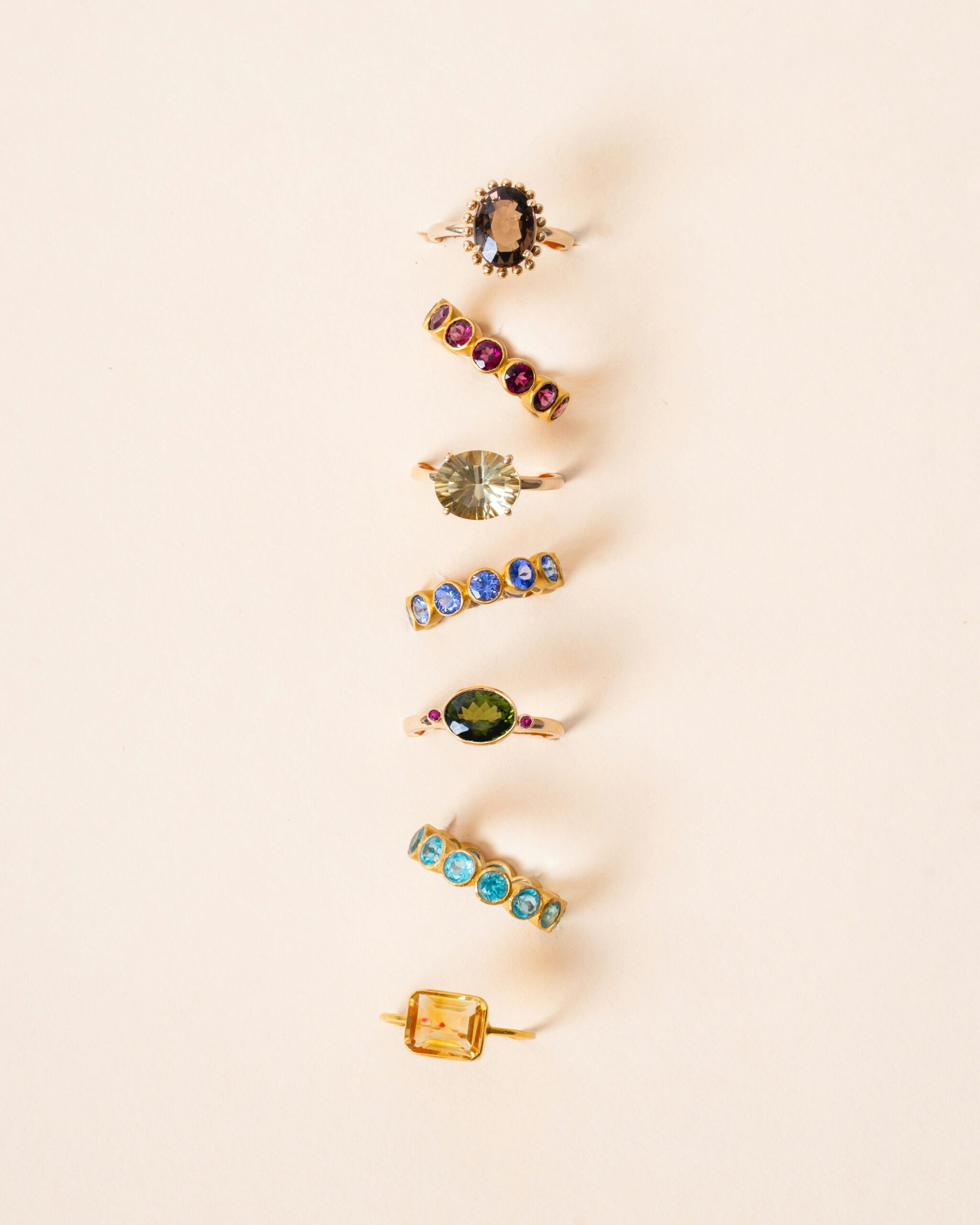 Home A stunning collection of gold rings featuring diverse gemstones, elegantly arranged on a beige background.